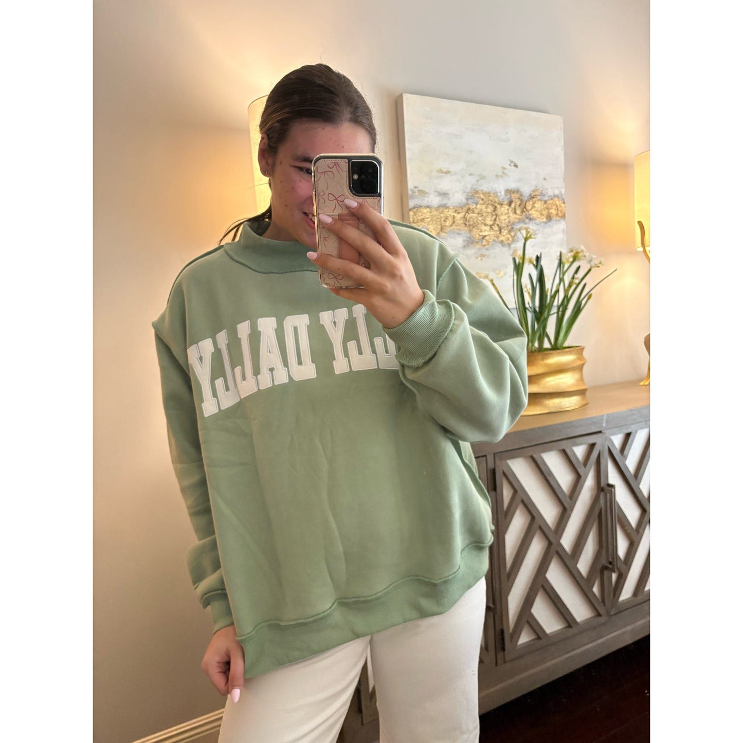 Person wearing a green sweatshirt with 'YLOLO' text, taking a mirror selfie in a room.