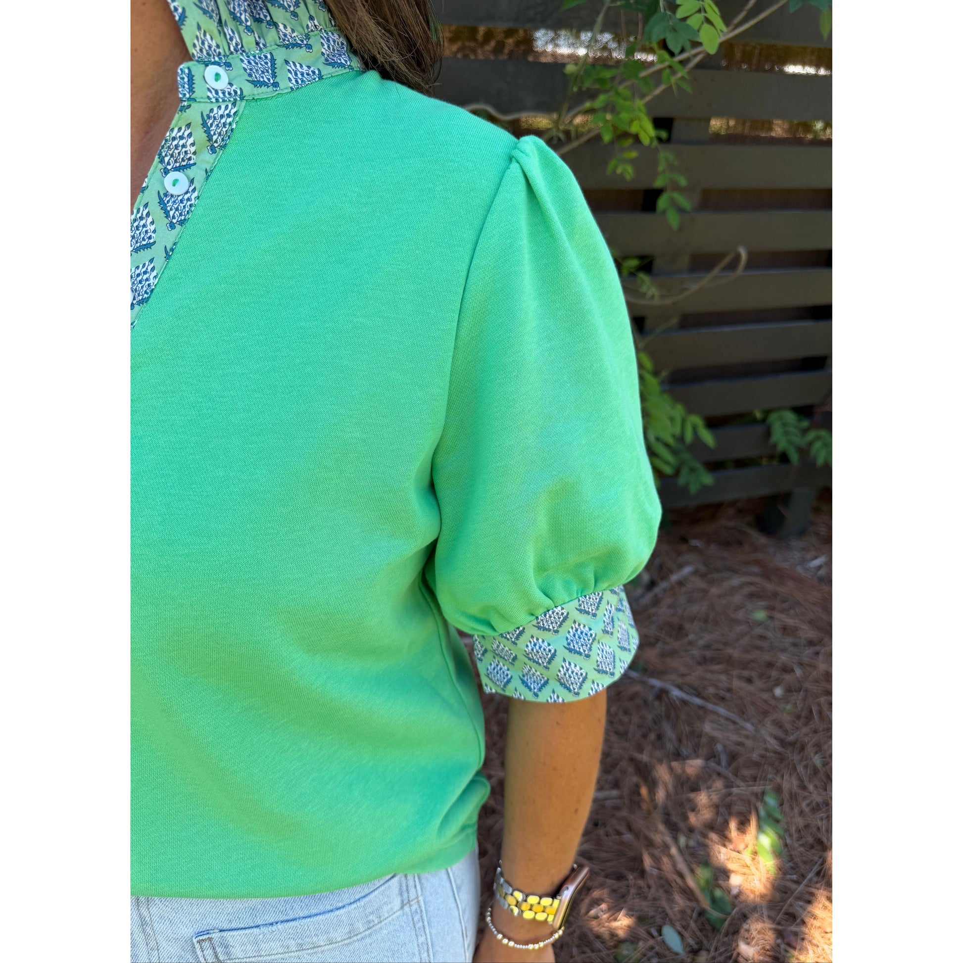 Person wearing a green top with patterned cuffs and hem, standing outdoors.
