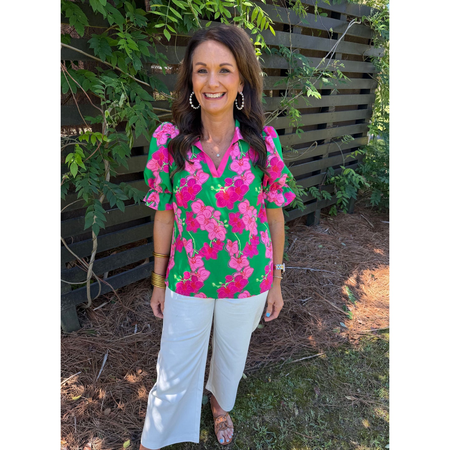 Woman wearing a colorful floral blouse and white pants standing outdoors.
