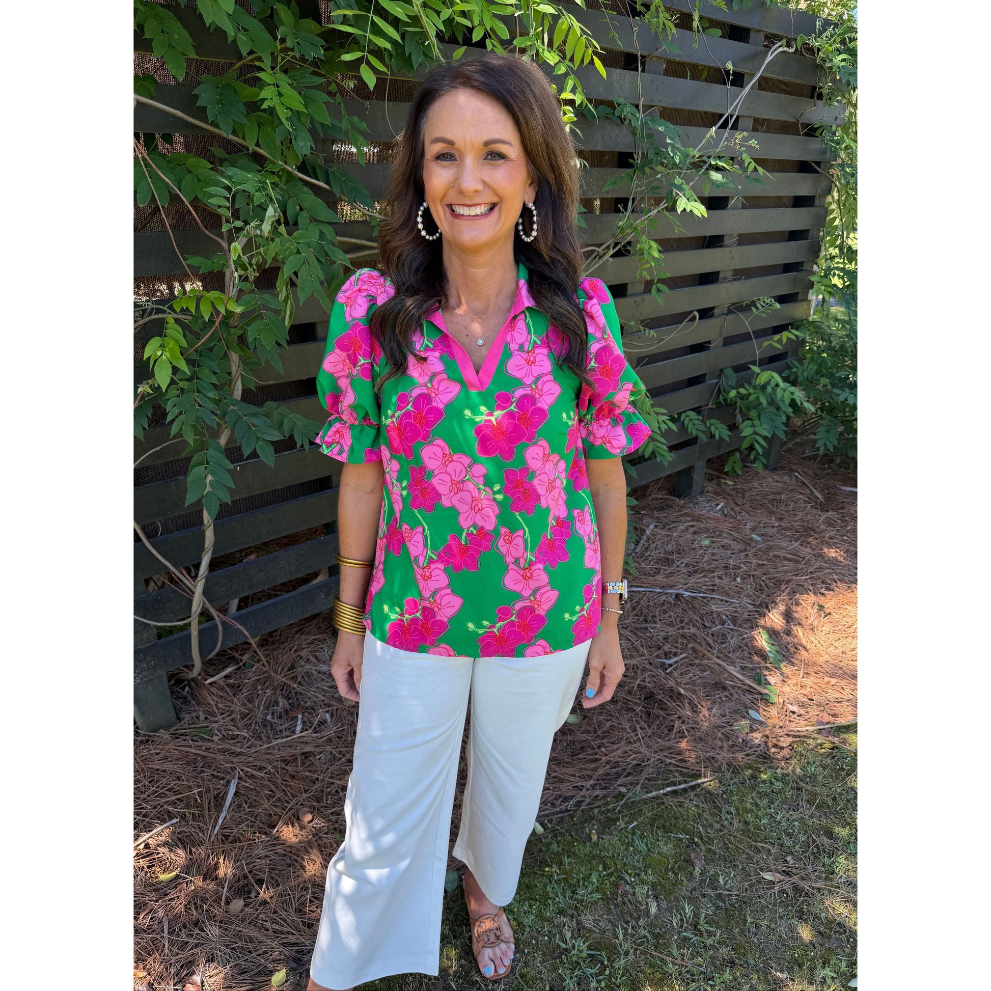 Woman wearing a colorful floral blouse and white pants standing outdoors.