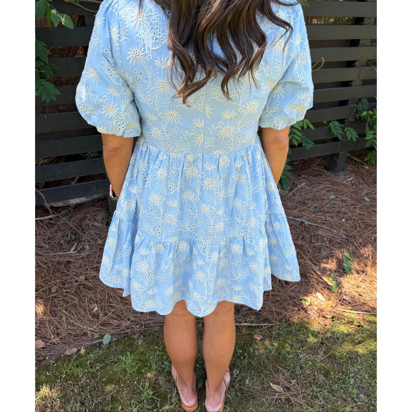 Person wearing a light blue dress with floral patterns outdoors.