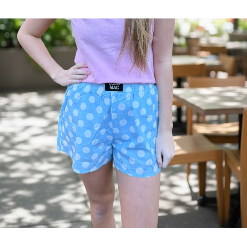 Young girl wearing a pink t-shirt and blue polka dot shorts standing outdoors.