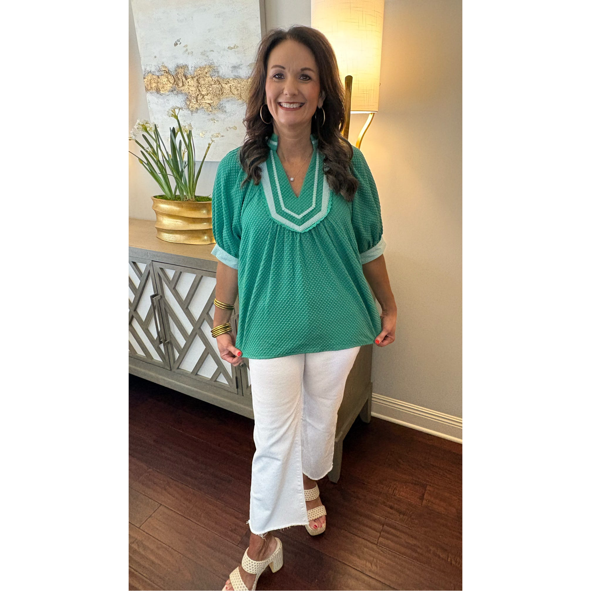 Woman wearing a green blouse and white pants in an indoor setting.
