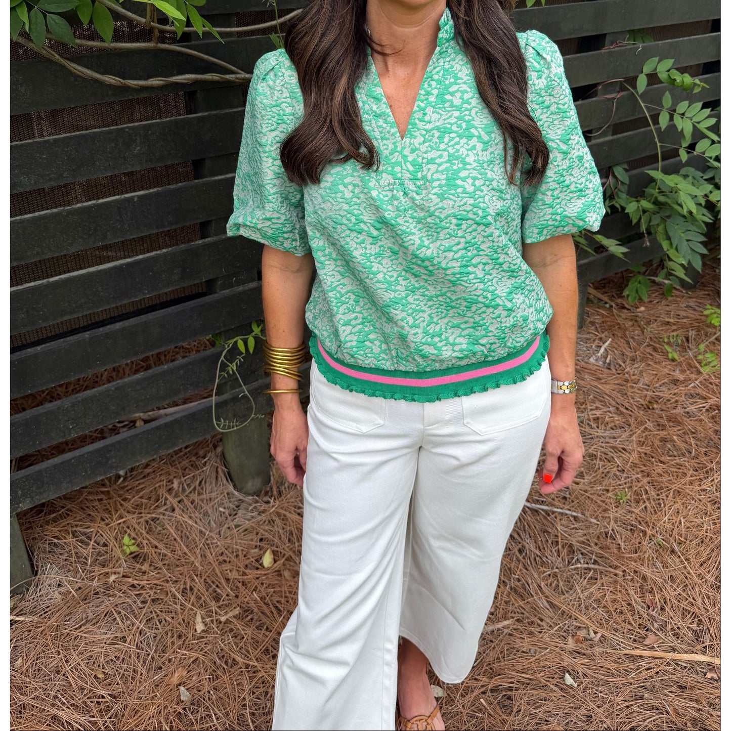 Person wearing a green patterned top and white pants standing outdoors.