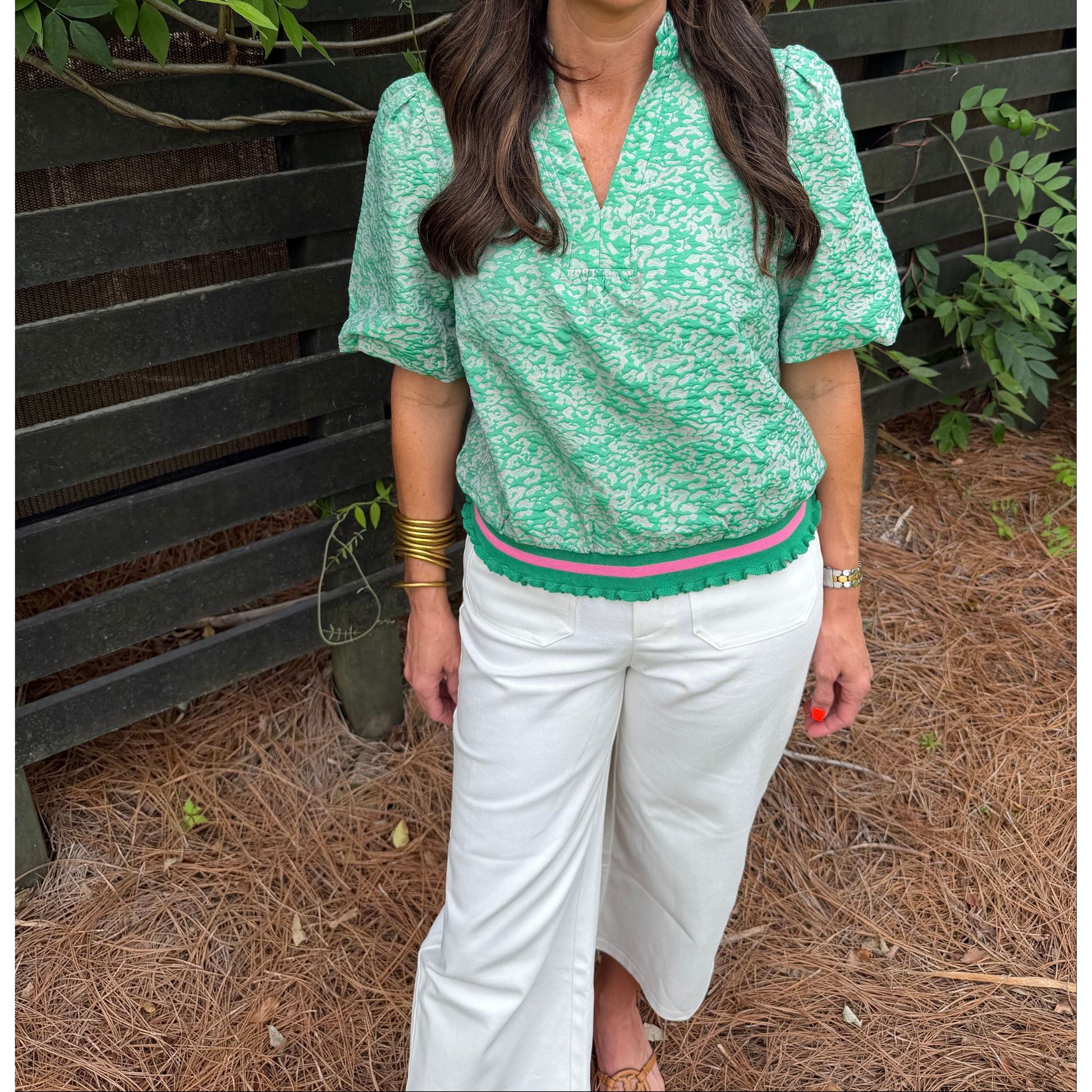 Person wearing a green patterned top and white pants standing outdoors.