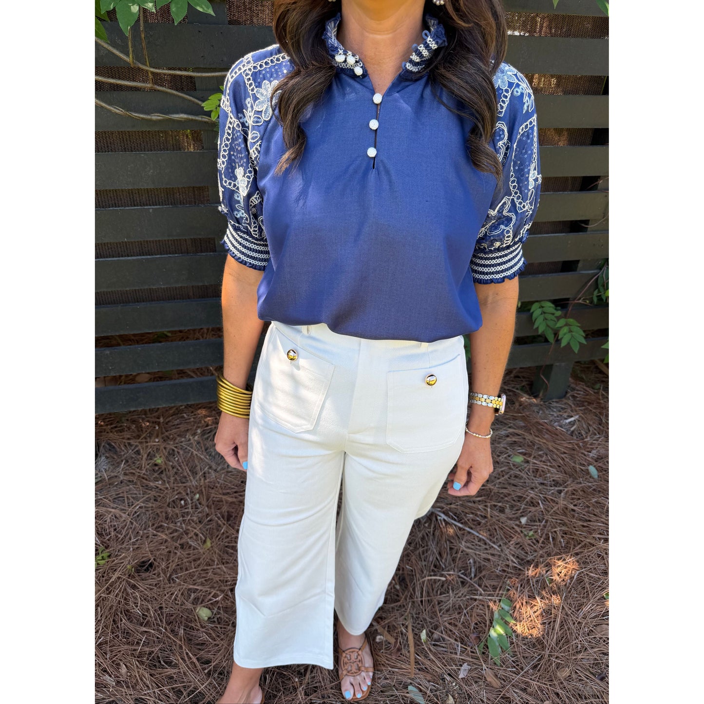 Person wearing a blue top and white pants sitting on a bench with a textured ground.