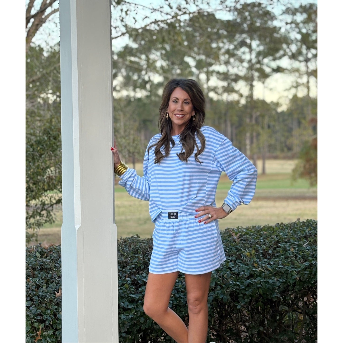 Woman in a blue and white striped outfit standing outdoors with trees in the background
