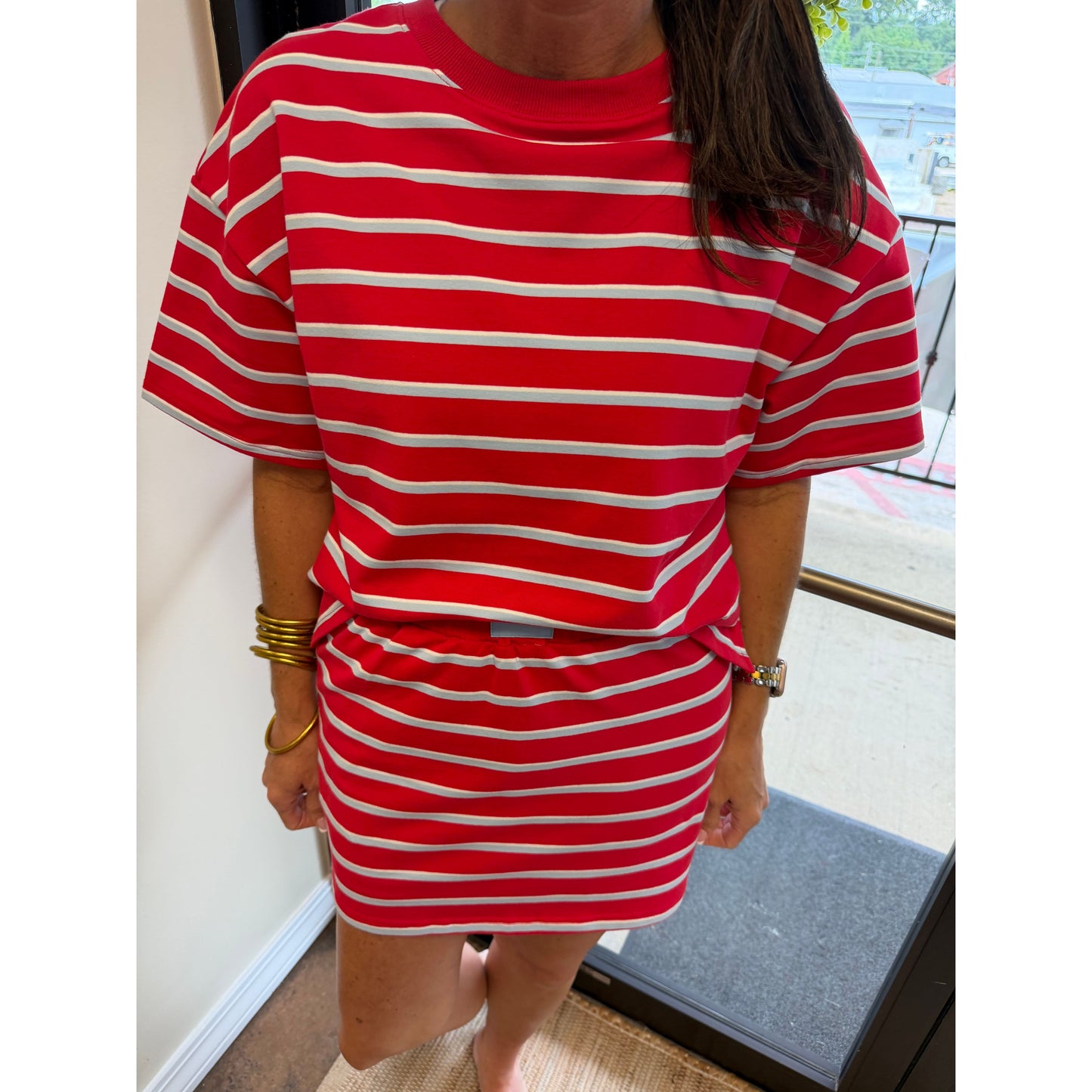 A person wearing a red and white horizontally striped short-sleeve t-shirt and matching striped mini skirt, standing indoors near a window.