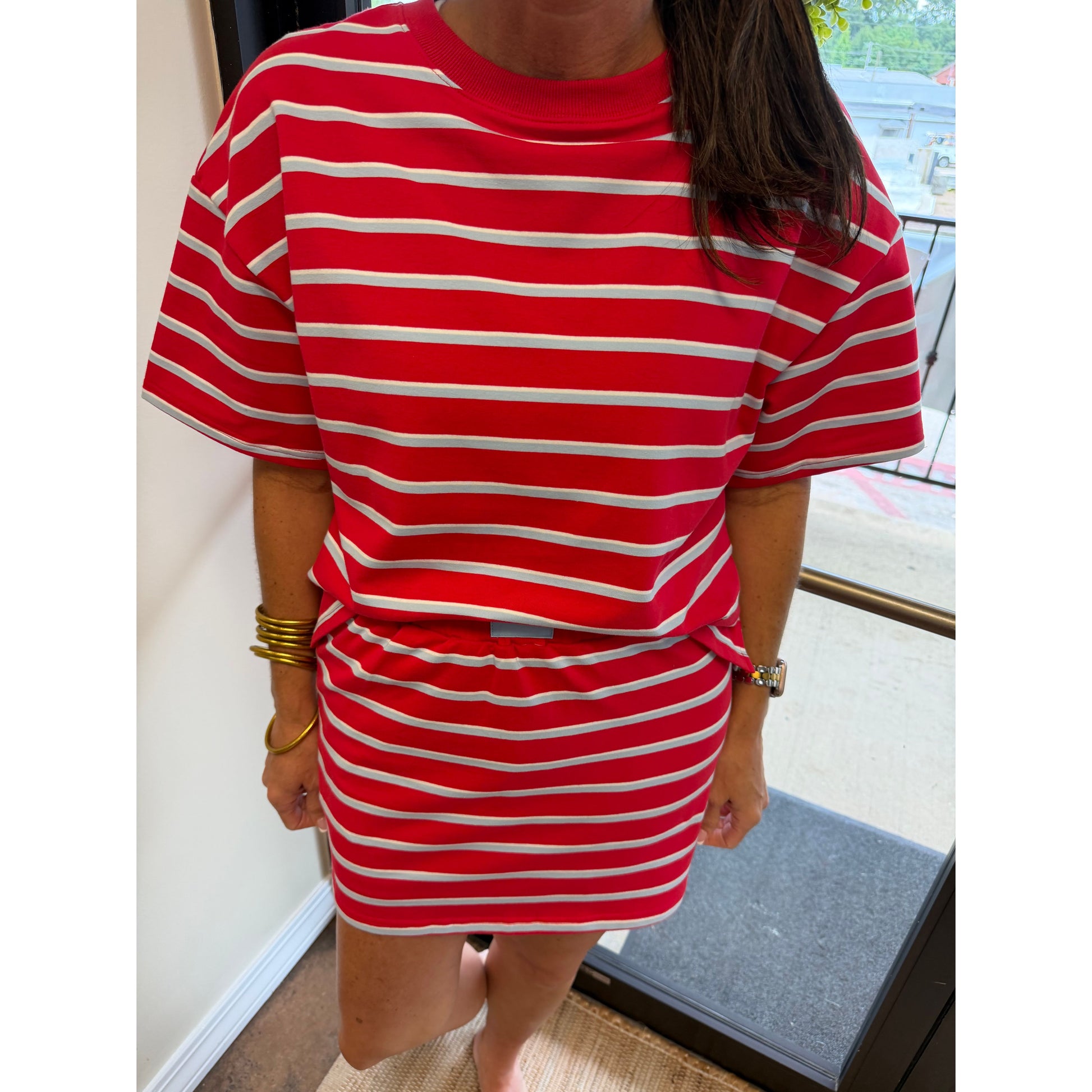 A person wearing a red and white horizontally striped short-sleeve t-shirt and matching striped mini skirt, standing indoors near a window.
