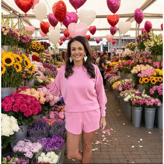 Woman in pink sweatshirt and shorts standing  in a flower market. 