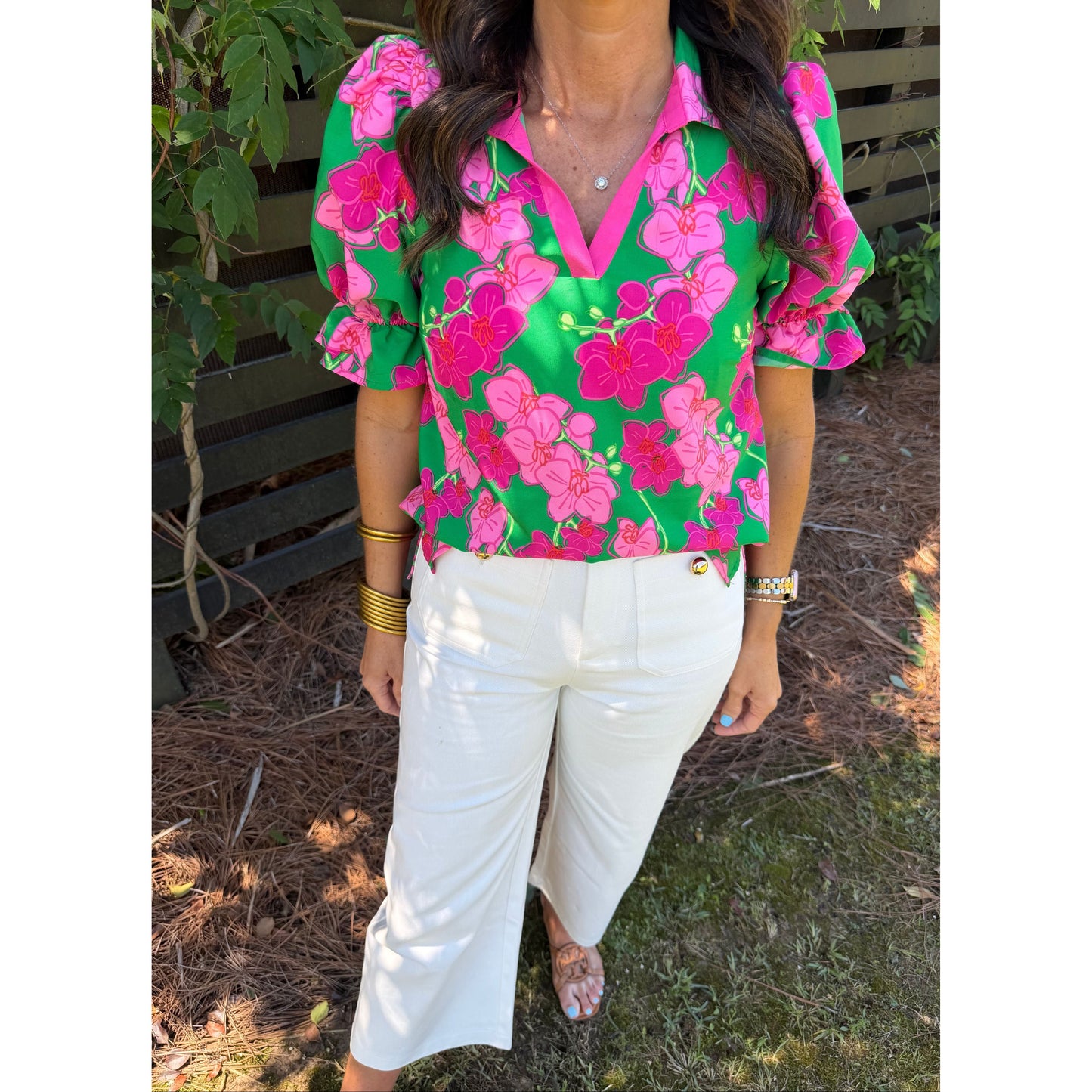 Person wearing a green and pink floral blouse with white pants outdoors.