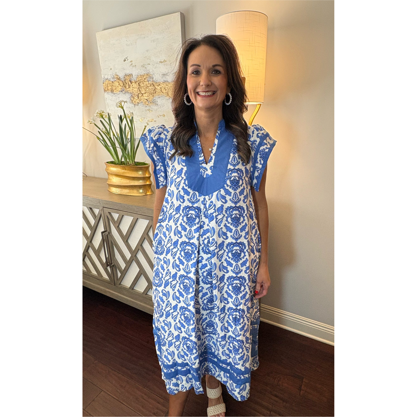 Woman wearing a blue and white floral dress in a room with decorative elements.