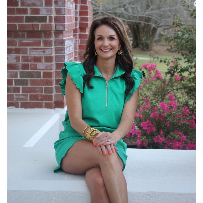 Woman in a green dress sitting outdoors with flowers and a brick wall in the background