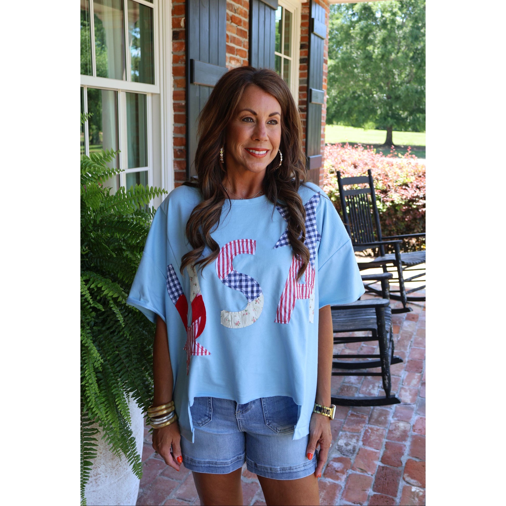 Woman wearing a light blue t-shirt with red and white graphics on a porch.