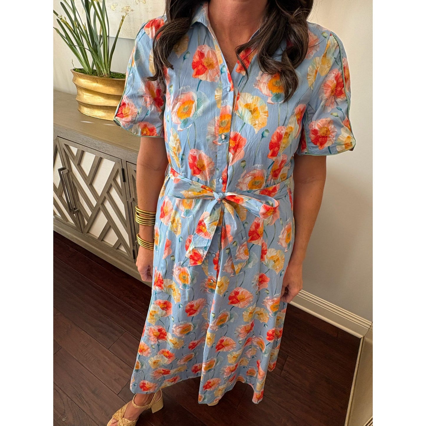 Woman wearing a floral dress with a plant and decorative cabinet in the background