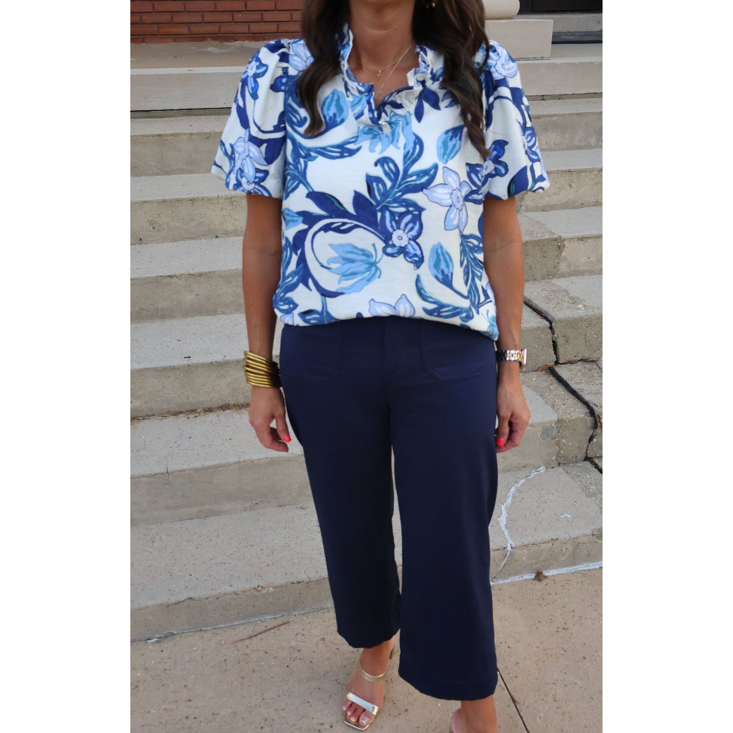 Person wearing a blue and white floral top with navy pants on a stone pavement.