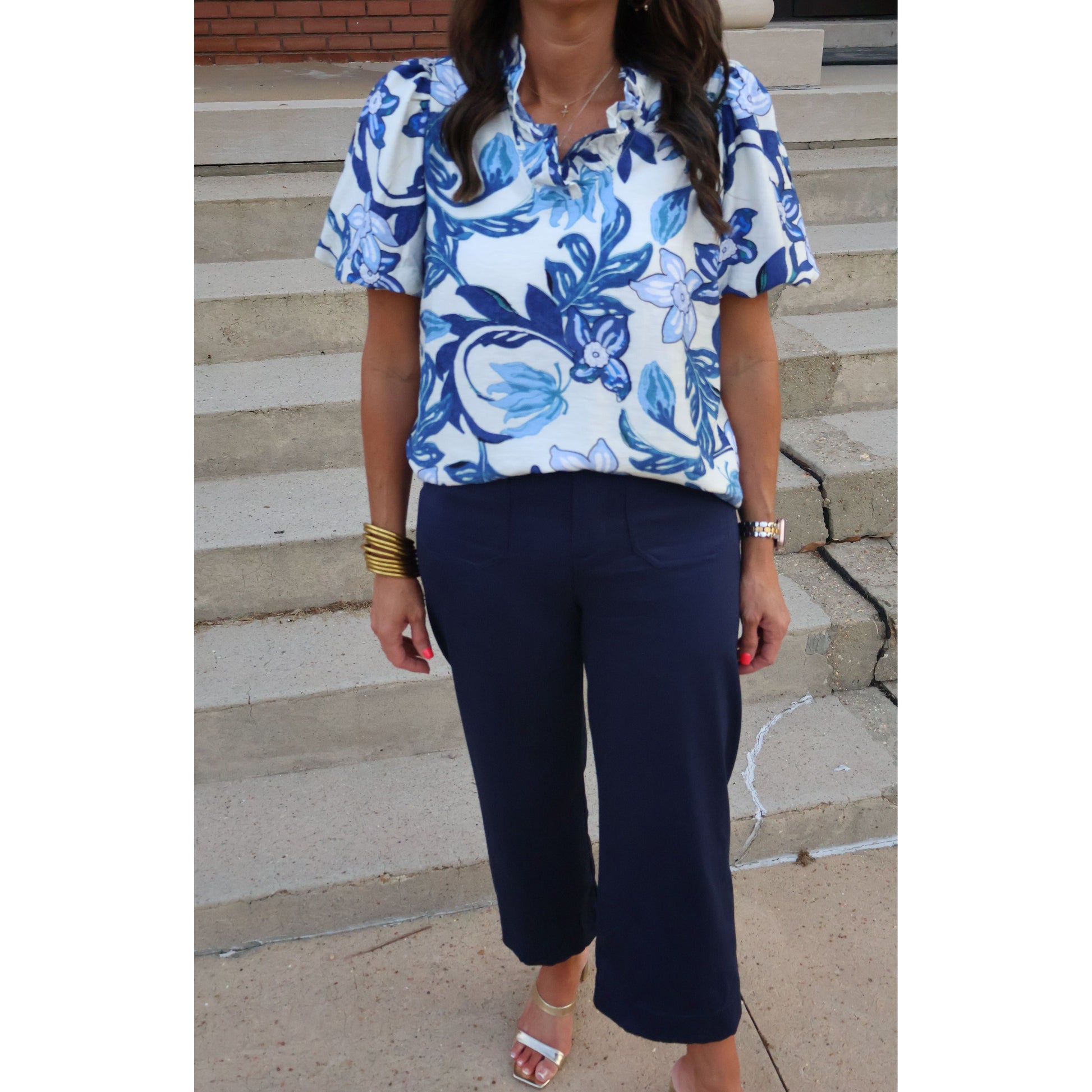 Person wearing a blue and white floral top with navy pants on a stone pavement.