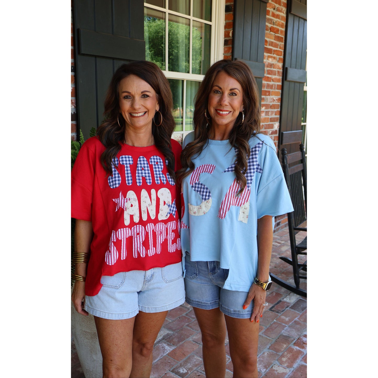 Two women standing outside a house, wearing red and blue t-shirts with text.