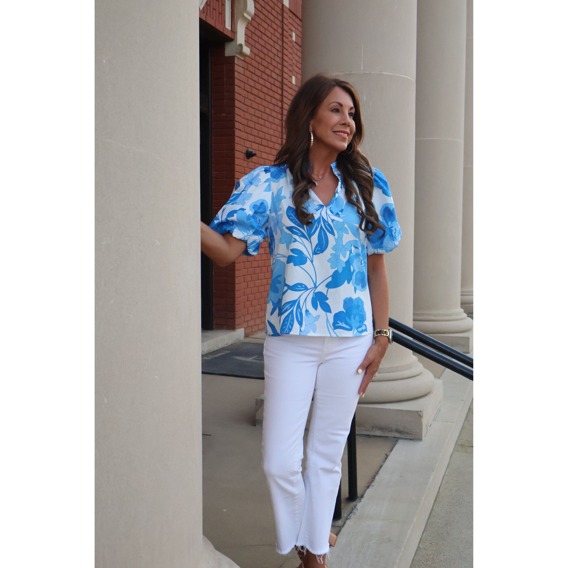 Woman wearing a blue floral dress and white pants standing in a room with a staircase.