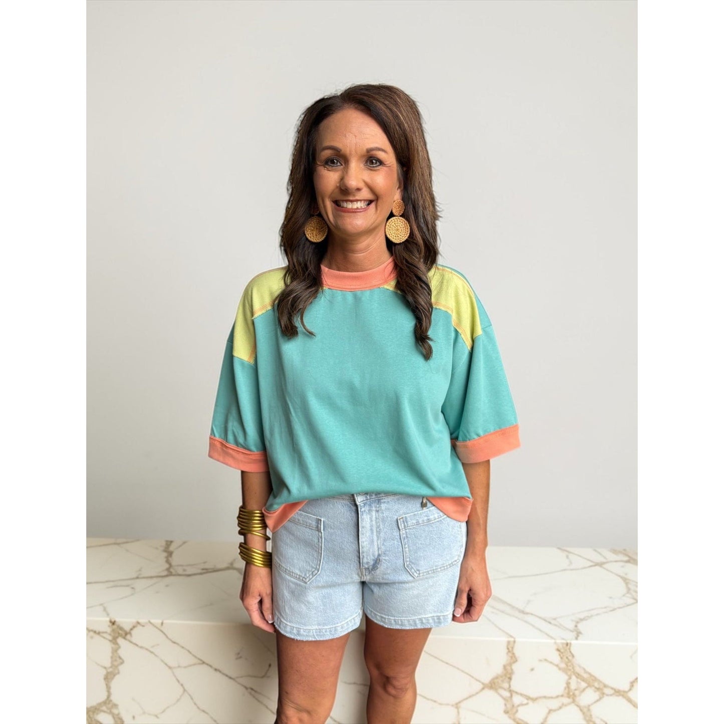 Woman wearing a colorful striped shirt and denim shorts on a marble surface with a neutral background
