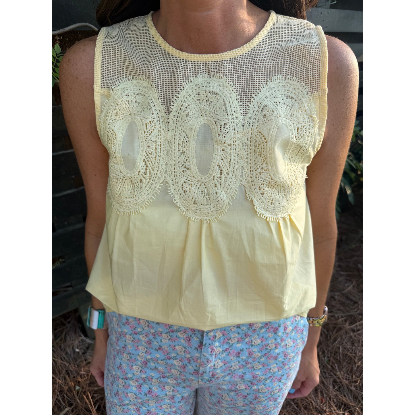 Person wearing a light yellow sleeveless top with lace details and floral pants.