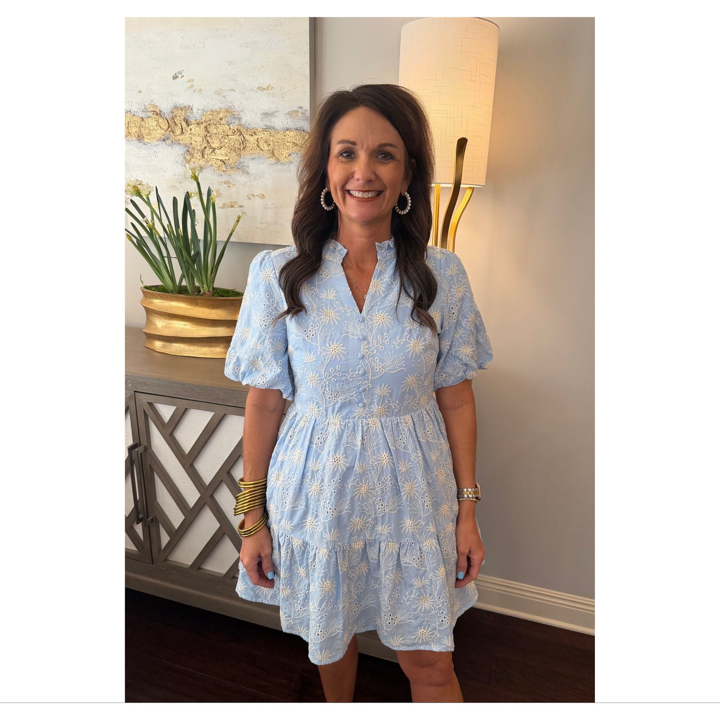 Woman in a light blue dress standing indoors with decor in the background