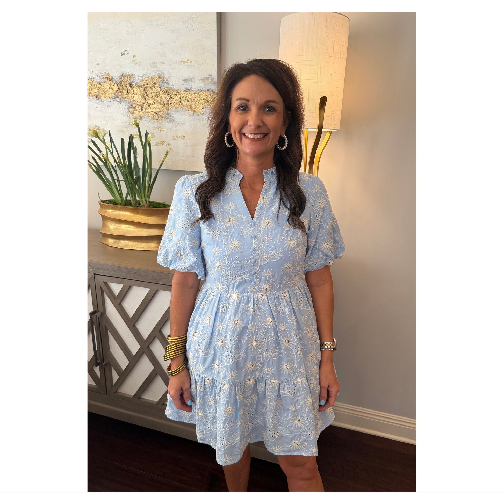 Woman in a light blue dress standing indoors with decor in the background