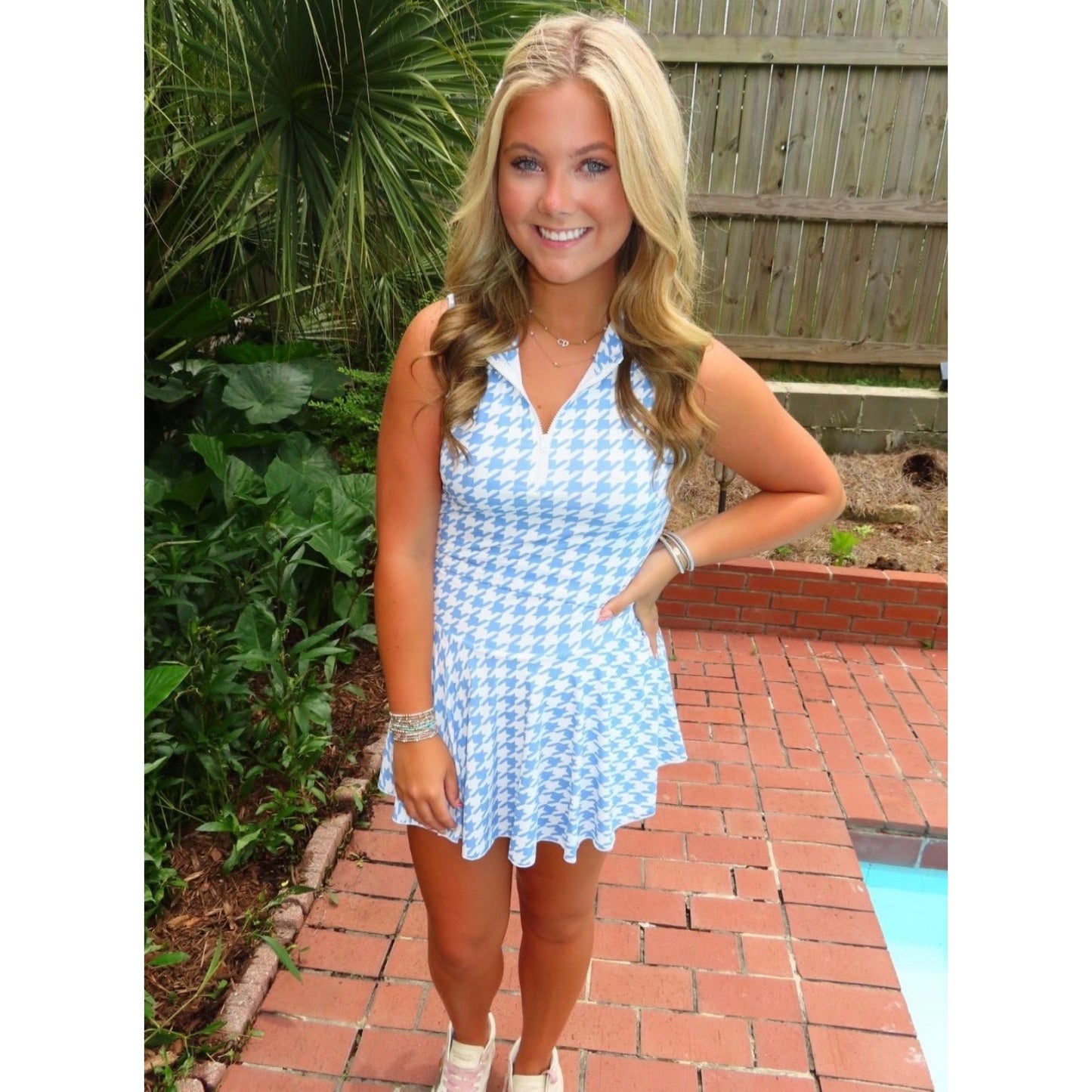 Woman in a blue checkered dress standing outdoors near a pool.