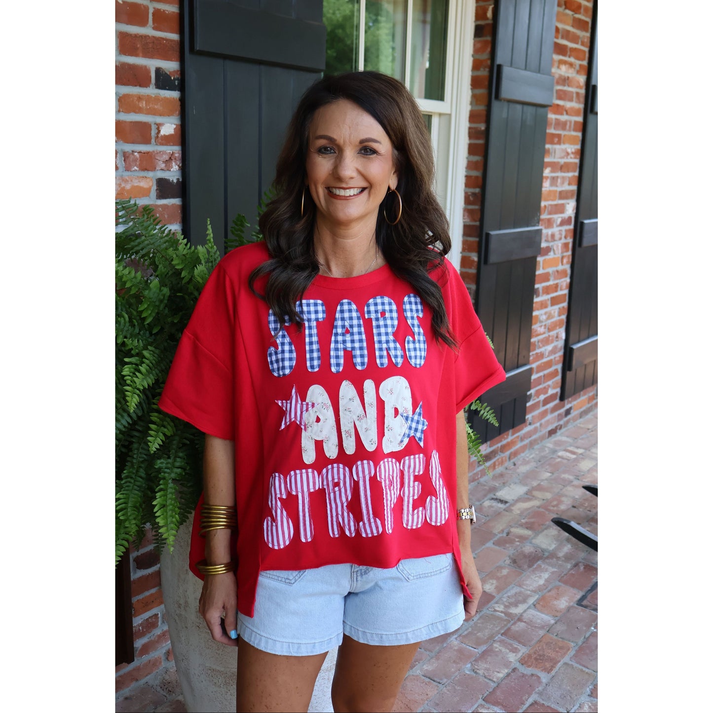 Woman wearing a red 'Stars and Stripes' shirt standing in front of a brick building.
