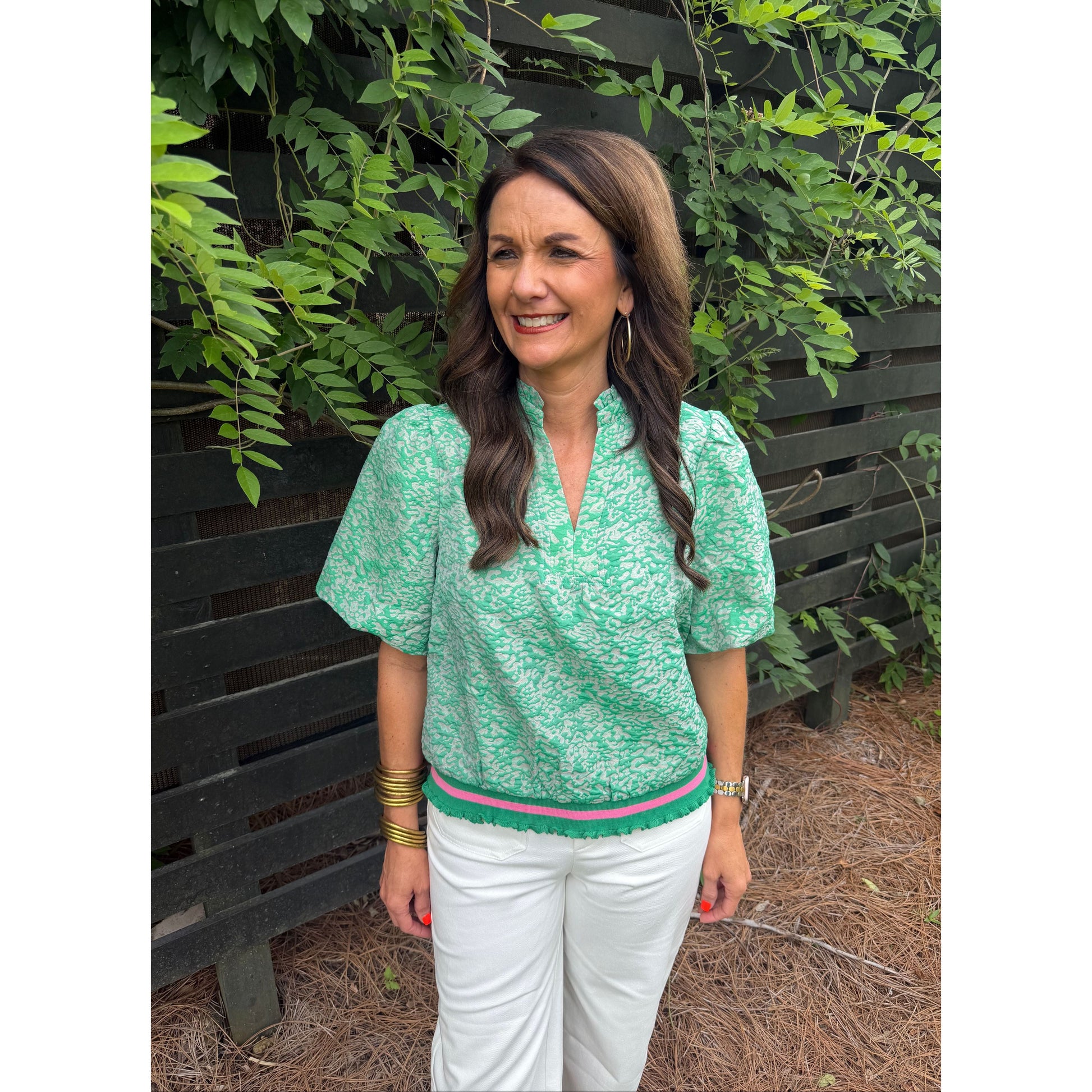 Woman in a green top and white pants standing outdoors with plants around