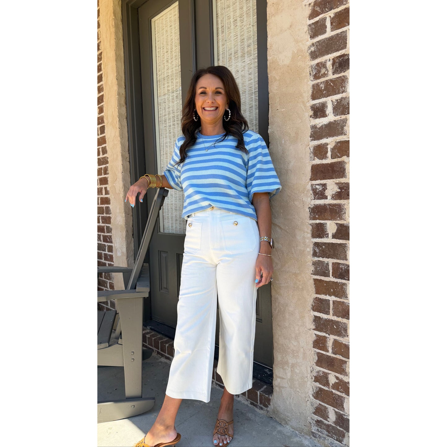 Person wearing a blue and white striped shirt and white pants standing on a sidewalk.