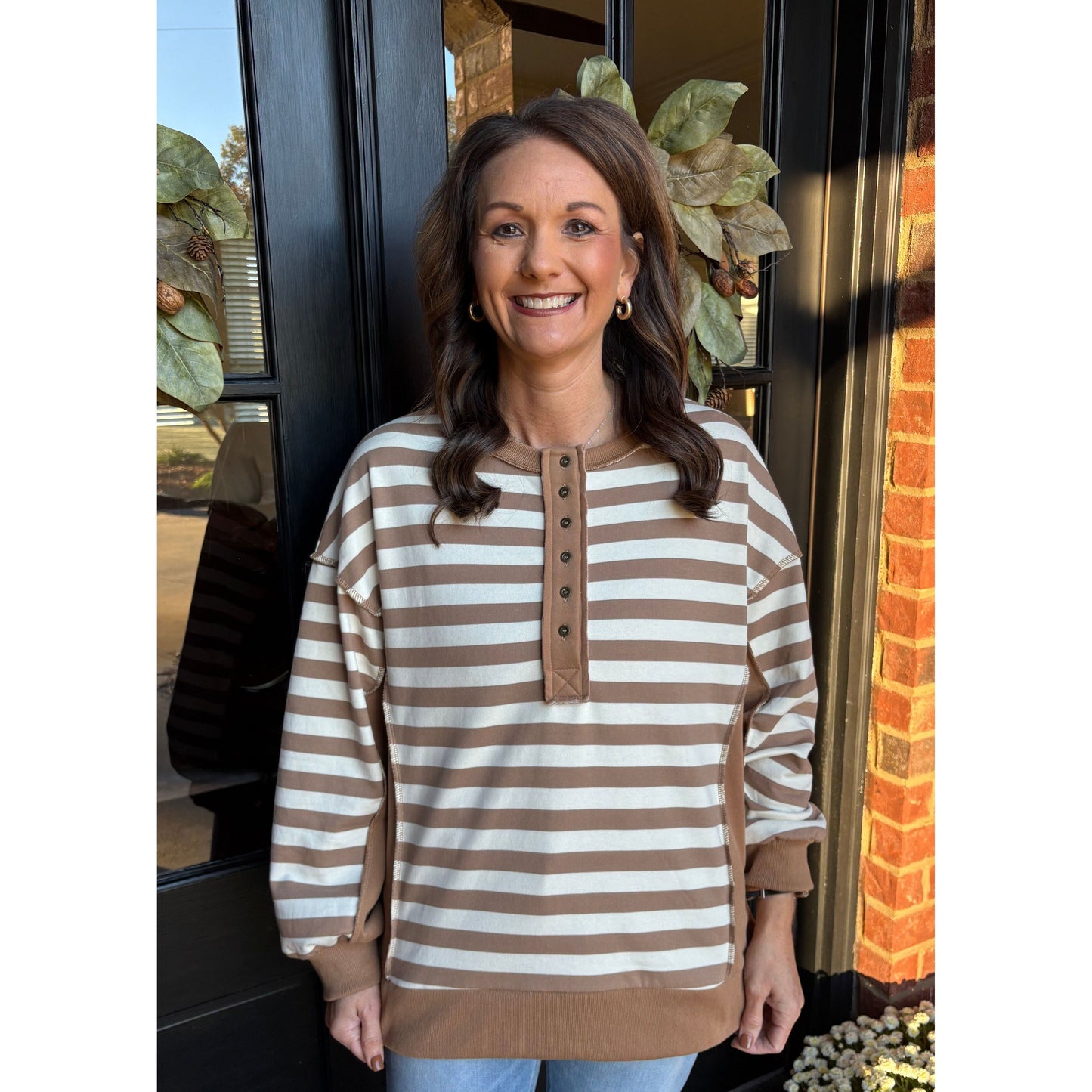 Woman wearing a brown and white striped sweater standing in front of a door with decorative elements.