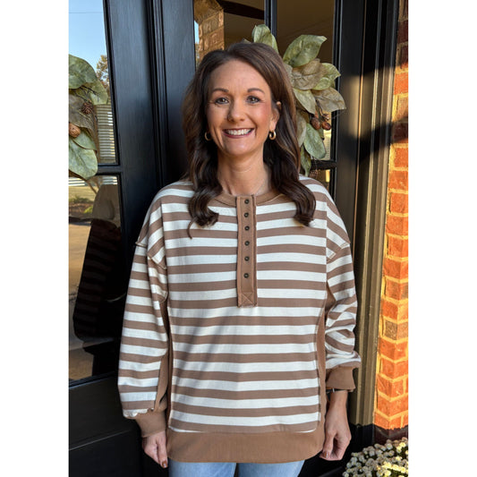 Woman wearing a brown and white striped sweater standing in front of a door with decorative elements.