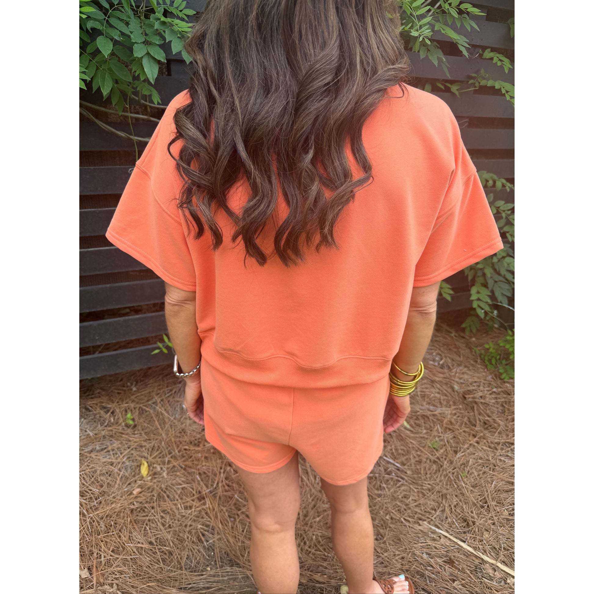 Person wearing an orange dress standing outdoors with plants in the background