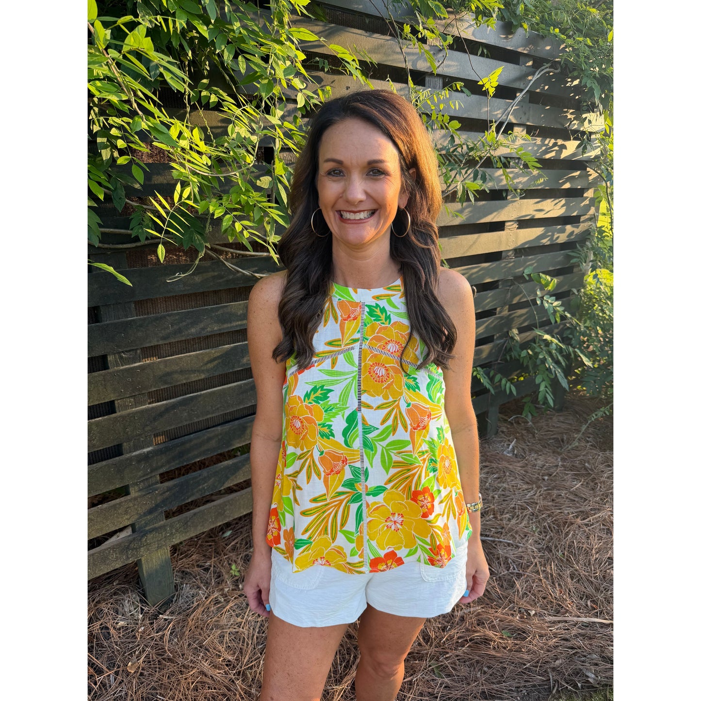 Woman wearing a colorful floral top standing in front of a wooden fence.