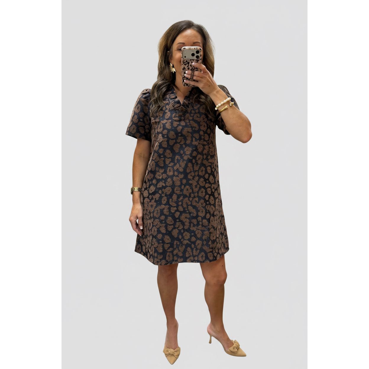 A woman takes a mirror selfie in a clothing boutique wearing a short-sleeve collared dress with a brown and black floral pattern.