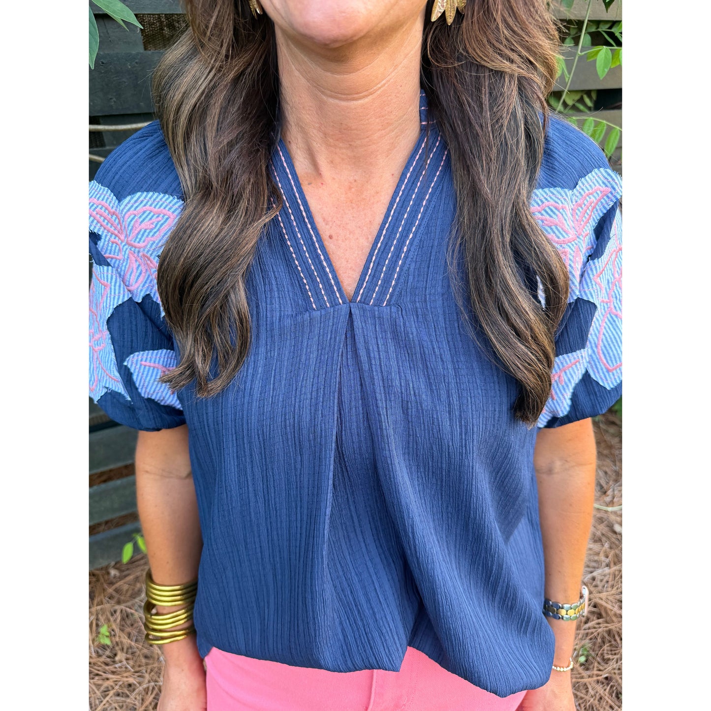 Woman wearing a blue blouse with pink accents, standing outdoors.
