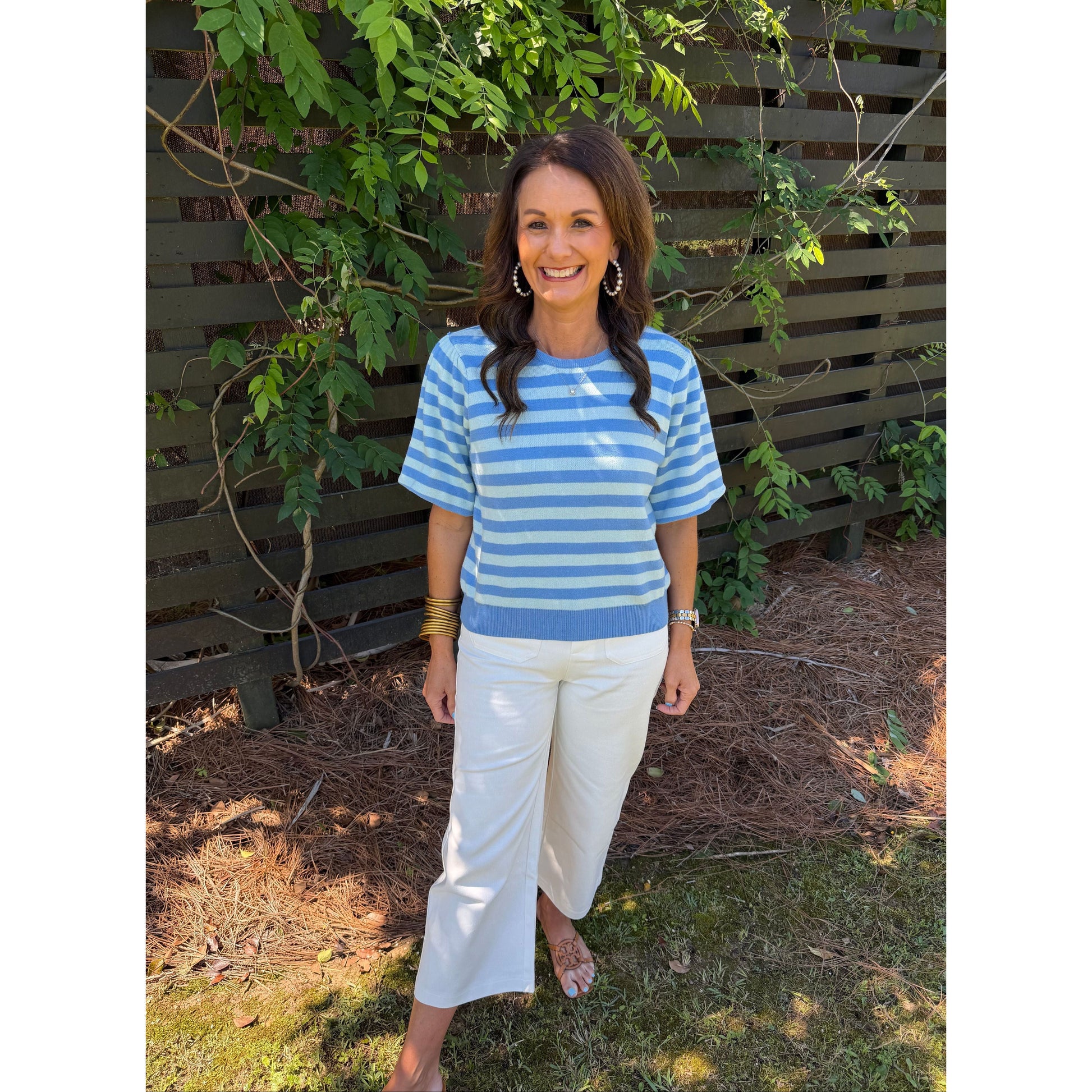 Woman wearing a blue and white striped shirt and white pants standing outdoors.