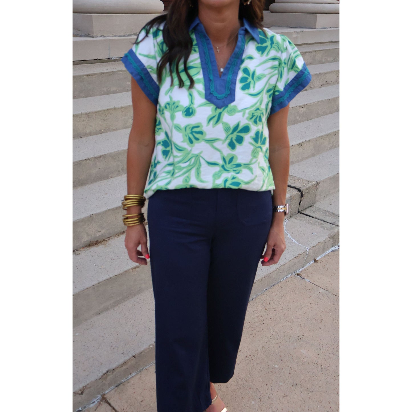 Person wearing a green and blue patterned top with navy pants on stone steps.
