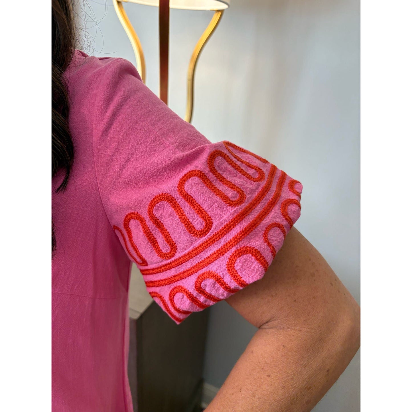 Person wearing a pink top with red patterned sleeves, standing indoors.