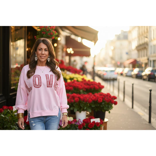 Woman wearing a pink sweatshirt with 'LOVE' printed on it, standing against a light-colored wall.