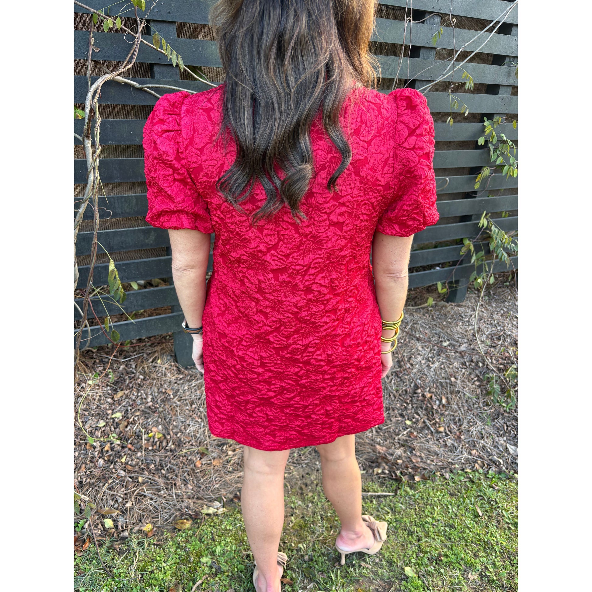 Person wearing a red textured dress standing outdoors on a bench.
