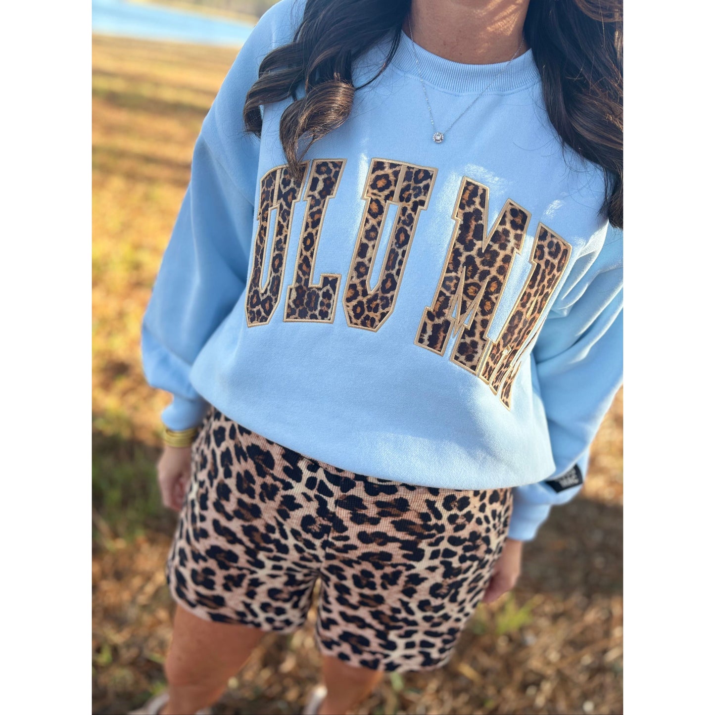 Person wearing a light blue sweatshirt with leopard print text and leopard print shorts outdoors.