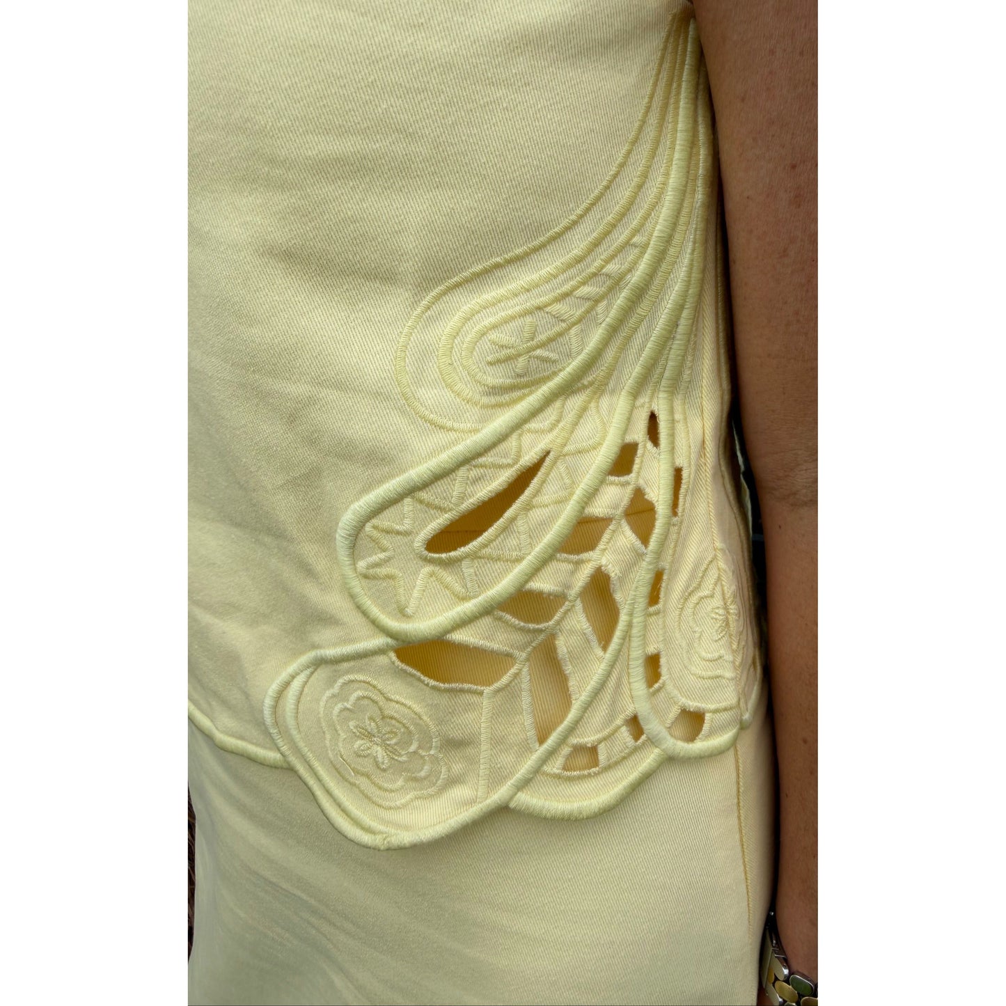 Close-up of a light-colored fabric with intricate patterns and a person's arm in the background.