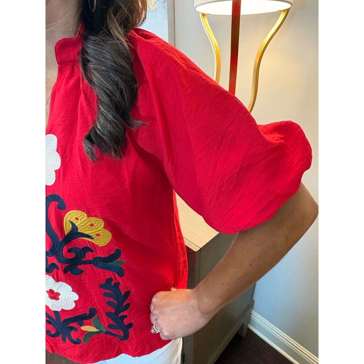 Person wearing a red embroidered top with floral patterns indoors.