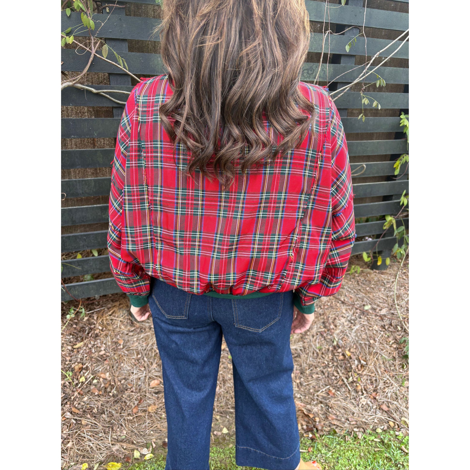 Person wearing a red plaid jacket and blue jeans sitting on a bench outdoors.