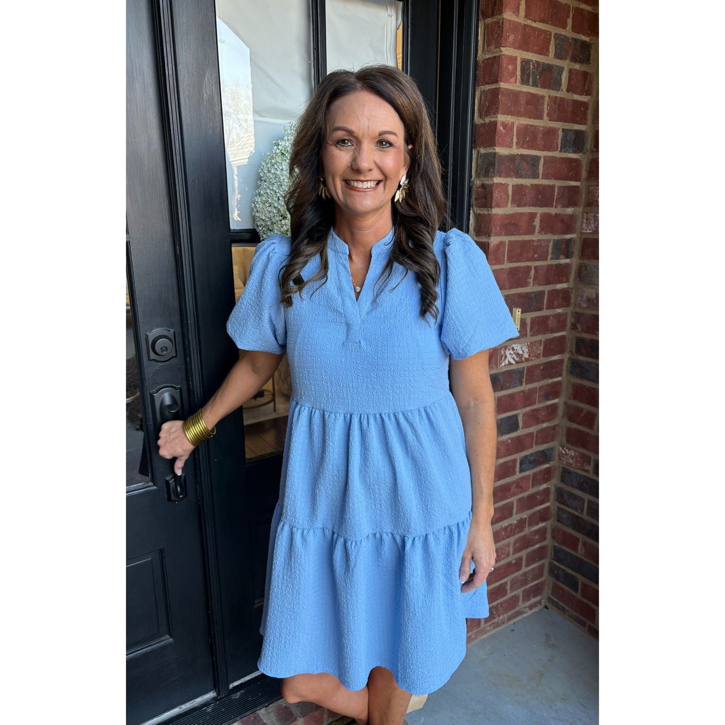 Woman in a blue dress standing in front of a black door with a brick wall background
