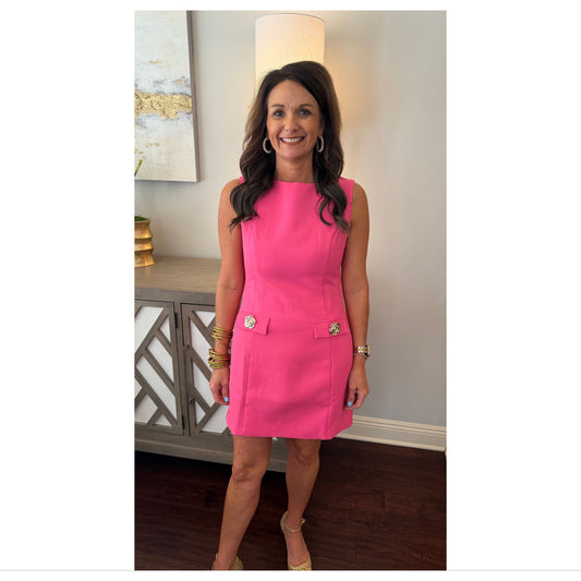 Woman wearing a pink dress standing in a room with a lamp and decorative items.