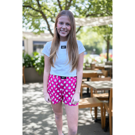 Young girl wearing a white t-shirt and pink polka dot shorts standing outdoors.