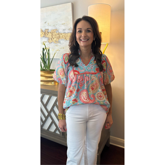 Woman wearing a colorful paisley blouse and white pants indoors.